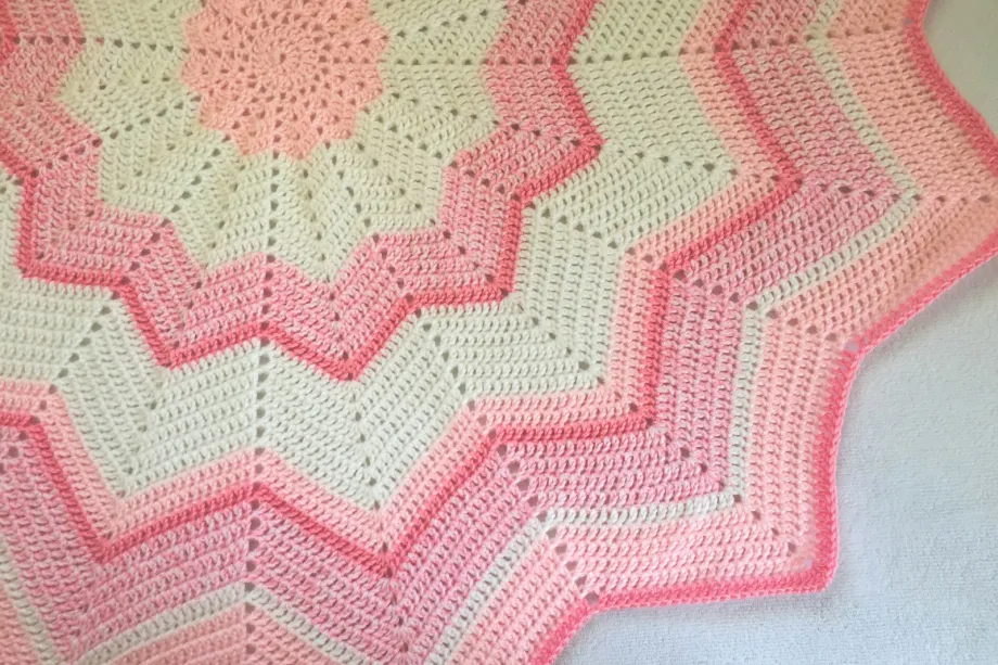 Pink and white crocheted blanket spread on a bed