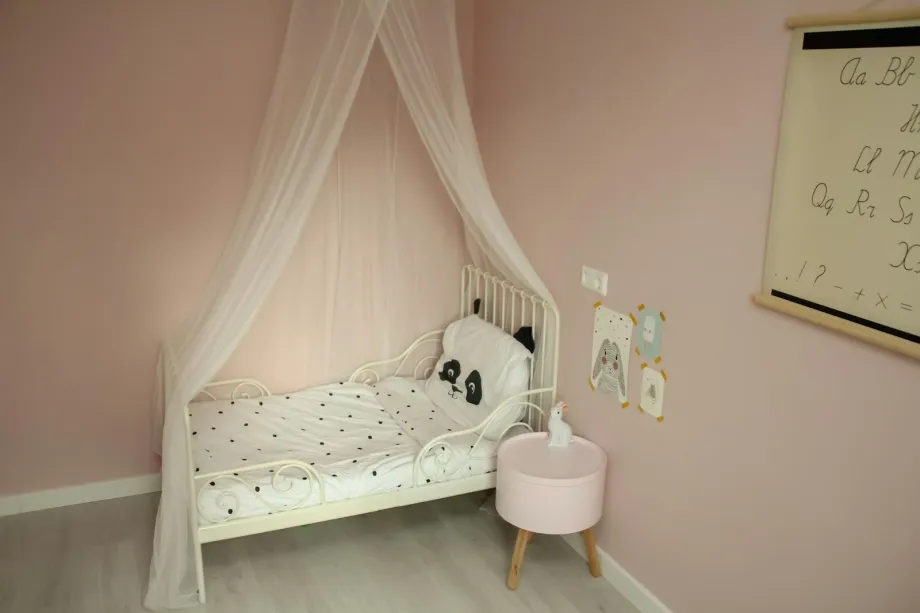Toddler bed with spotted bedding under a sheer canopy in a pale pink room