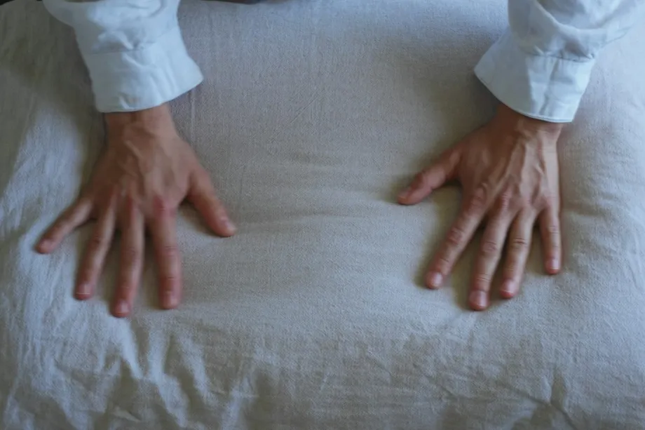 A person smoothing a fitted sheet over a mattress in a bright bedroom, ensuring the corners are tucked in securely.